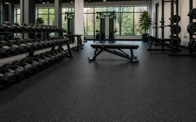 Weight room with racks and plates on a seamless black poured rubber floor.