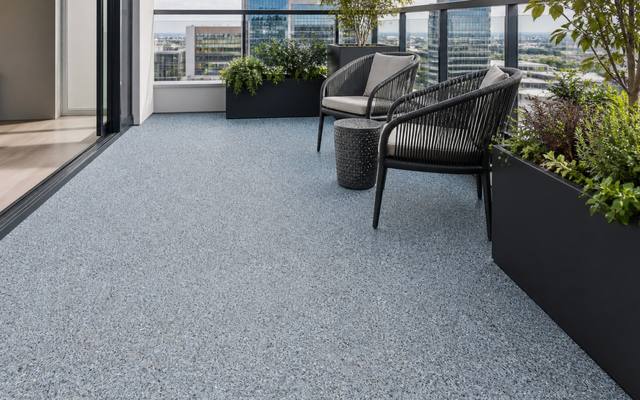 Condo balcony finished in grey rubber surfacing with patio chairs and planters.
